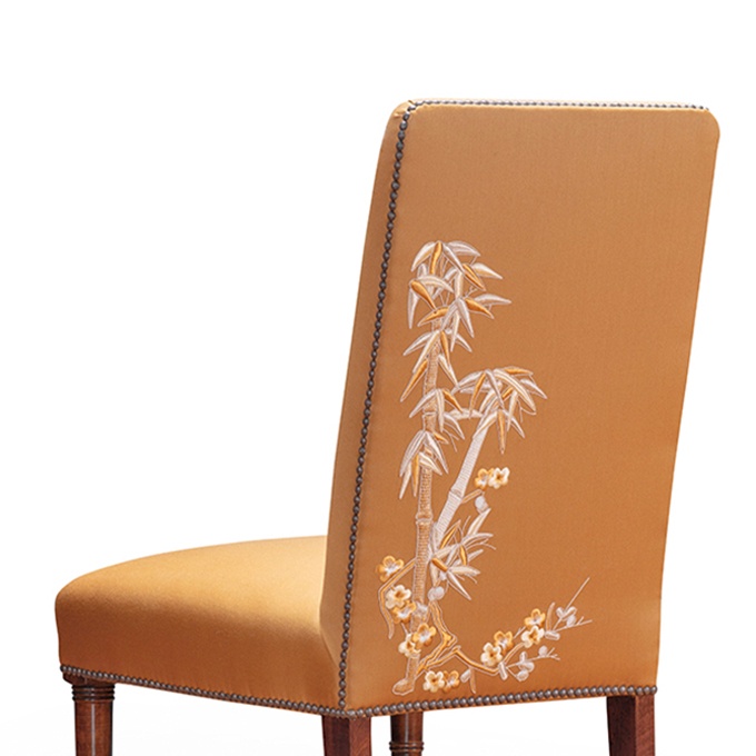 A luxurious upholstered chair with hand embroidered palm trees.