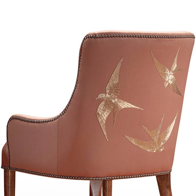 A luxurious upholstered dining chair with hand embroidered birds on the back.